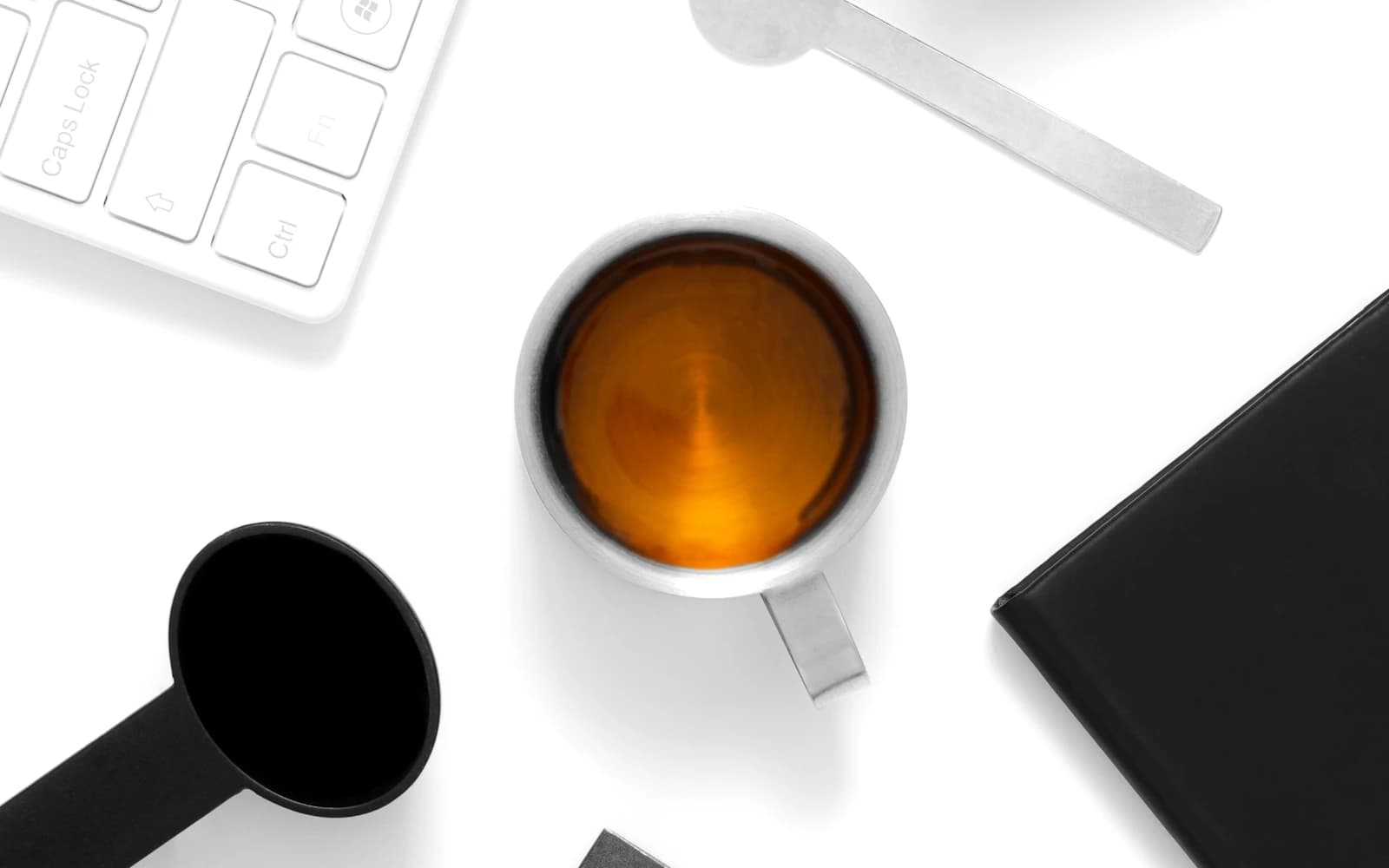 A phone, coffee cup, keyboard, and notebook arranged on a white desk